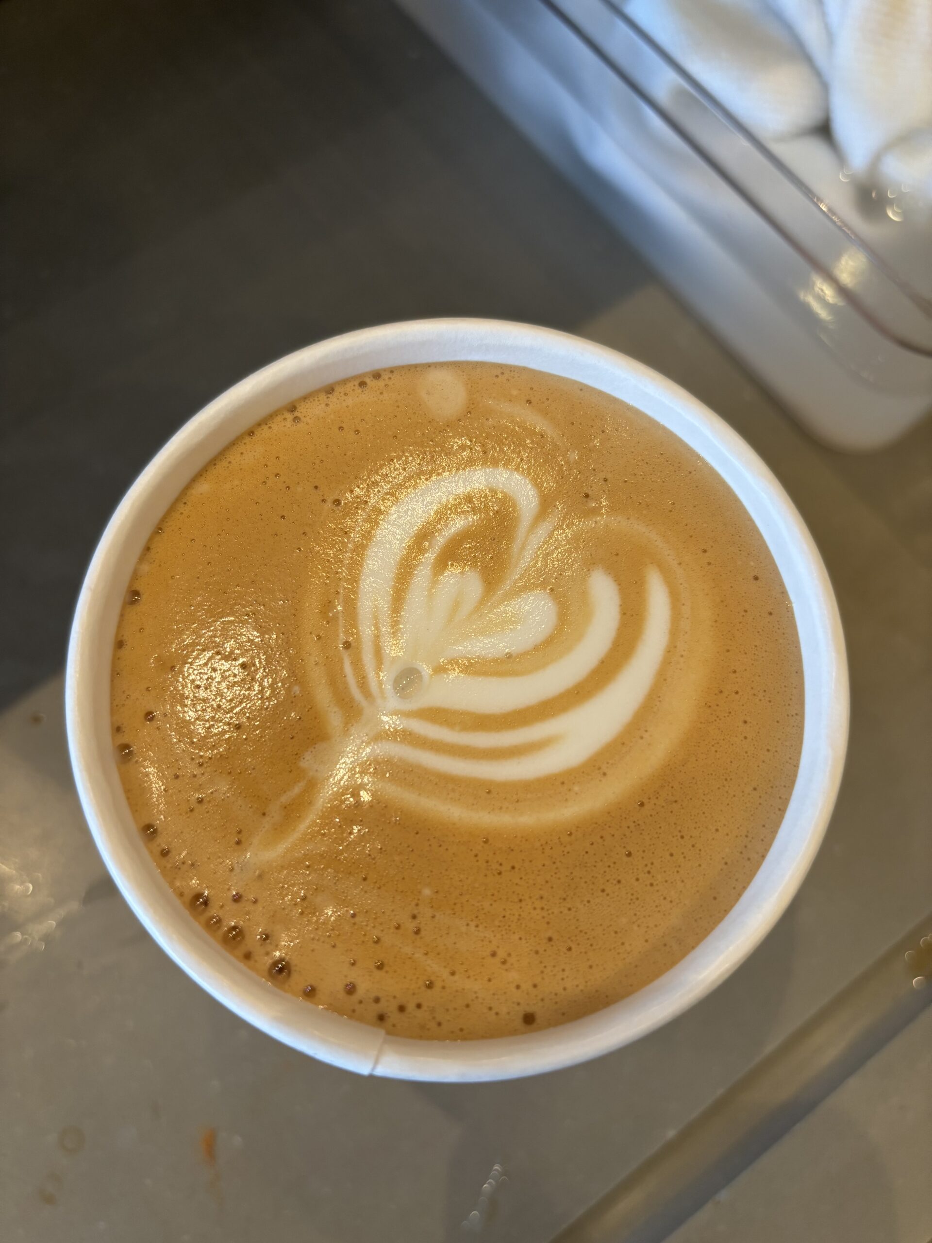 A top-down view of a latte with a heart-shaped foam art design in a white paper cup, representing the attention to detail and creativity developed in the service industry.